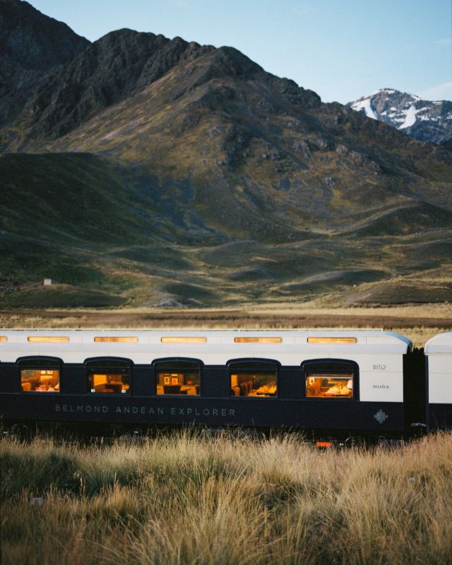 dark blue and white Belmond Andean Explorer train with mountain in the background
