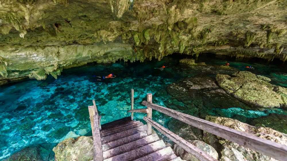 wooden stairway going down the body of water inside the cave with people swimming around- Amazing Things to Do in Mexico's Yucatan Peninsula