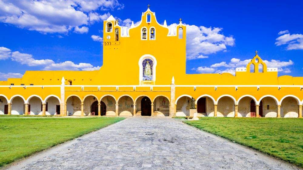 yellow building with virgin Mary statue on the middle surrounded by green grass- Amazing Things to Do in Mexico's Yucatan Peninsula