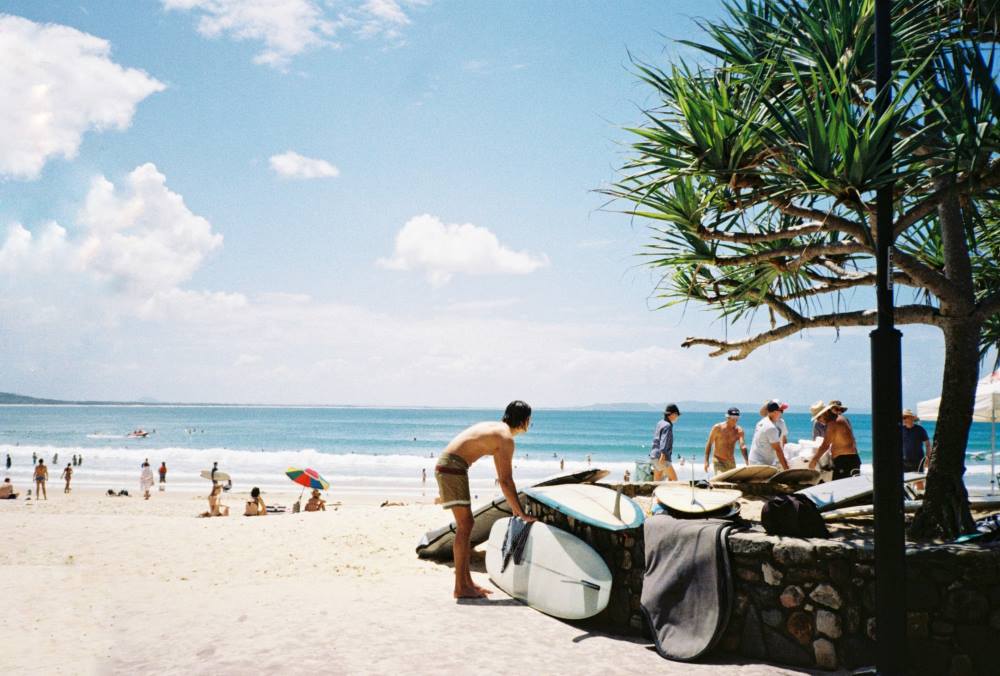 man holding a surf board with people around the sand near the beach