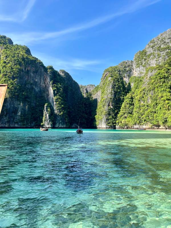 boat in the middle of crystal clear ocean with rock formation in the back -phuket vs krabi
