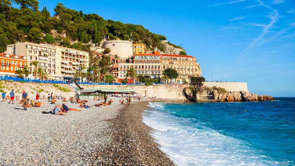 people sitting in the sand in front of the beach - Things to do in Nice, France