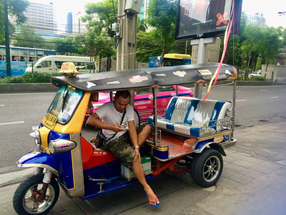 man looking down on his phone inside a tuktuk ride