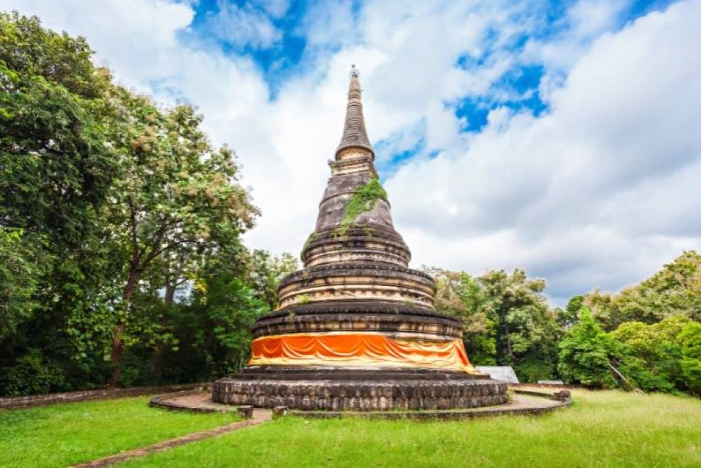 brown concrete structure in the middle of the park surrounded by green grass and trees- chiang mai temples